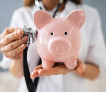 Midsection Of Young Female Doctor Holding Piggybank In Clinic